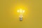 Glowing classic light bulb with filament on yellow background