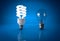 Glowing energy saving bulb and dead incandescent bulb over bluebackground