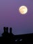 Glowing full moon in a purple twilight summer sky above a house rooftop in silhouette