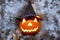 Glowing Halloween pumpkin in woolen hat on heap of leaves. Puffs of smoke