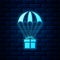 Glowing neon Gift box flying on parachute icon isolated on brick wall background. Delivery service, air shipping concept