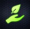Glowing neon Hand hold a leaf of the plant icon isolated on brick wall background. Care nature. Leaf shoots with