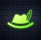 Glowing neon Oktoberfest hat icon isolated on brick wall background. Hunter hat with feather. German hat. Vector