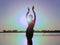 Glowing silhouette of slim woman with hands up in the air illuminated with sunshine dancing traditional tribal belly dance in fron