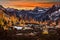 Glowing tents in mountains among snow capped peaks and golden trees.