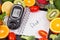 Glucometer with result of sugar level, fruits with vegetables and notepad with word diet. Healthy food for diabetic concept