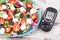 Glucometer with sugar level and greek salad with feta cheese and vegetables. Best food for diabetics, dieting and slimming