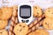 Glucose meter for measuring sugar level and heap of cookies, concept of reduction eating sweets