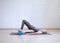 Gluteal bridge on foam roller. Young caucasian woman doing pilates with special equipment in fitness studio.
