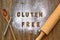 Gluten free flour with text gluten free in English language with wooden spoon, beater and rolling pin on dark brown wooden backgro