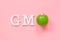 GMO tex from white volume letters and green apple on pink background. Concept of genetically modified foods or fruits. Top view