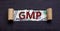 GMP symbol. The word `GMP - good manufacturing practice` appearing behind torn black paper. Beautiful background from dollar bil