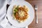 GNOCCHI COOKED WITH GROUND MEAT IN TOMATO SAUCE, COVERED IN GRATED CHEESE MOUNTED ON A WHITE PLATE ON A WOODEN BACKGROUND