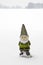 Gnome with green suite and hat standing in country field of snow