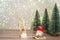 A gnome in a white hat leads a gnome in a red hat on a sleigh. Winter background Christmas trees in sparkles and a deer