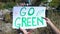 Go green phrase on cardboard in person hands against open dumping background