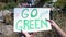 Go green phrase on cardboard in person hands against open dumping background