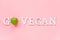 Go vegan healthy diet concept. Green natural fresh apple in word Go Vegan from white letters on pink background. Creative flat lay