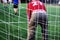 Goal net behind goalkeeper in red uniform. Everyone plays football