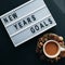 `GOALS` text on desk and cup of cocoa on black background, top view, flat lay