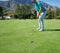 This is going straight in. a focused young man hitting a golfball with a putter into a hole on a golf course.