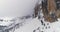 Going up rising aerial with snowy mountain,road and woods forest at Sella pass.Cloudy bad overcast foggy weather.Winter