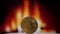 A gold bitcoin coin slowly spinning against the background of a burning fire.