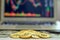 Gold bitcoins and dollar bills appearing from above a laptop with stock exchange charts on the screen