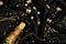 Gold Champagne bottle with confetti stars and party streamers on festive black background.