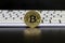 The gold coin of the bitcoin stands on the black background in front of the white keyboards