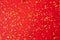 Gold confetti on red paper background. Festive holiday backdrop. Birthday congratulations Christmas New Year. Valentines Day. Flat