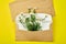 Gold envelope with a spring flower arrangement on yellow background. Flat lay, top view. Opened envelope.