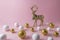 Gold glitter reindeer with gold and white glitter ball decoration on pink background.