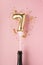 Gold inflatable number 7 on a stick with gold confetti on a pink background