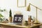Gold lamp, laptop and plant on wooden desk in white freelancer`s interior with poster. Real photo