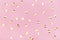 Gold metallic confetti on pastel pink background.