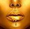 Gold paint drips from the lips, golden liquid drops on beautiful model girl`s mouth, creative abstract makeup