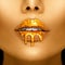 Gold paint drips from the lips, golden liquid drops on beautiful model girl`s mouth, creative abstract makeup