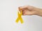 Gold ribbon hanging on fingers on white background. International Childhood Cancer Day concept