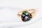 Gold ring decorated with a large gem, iridescent in different colors on a white silk fabric