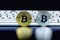 The gold and silver coins of the bitcoin stands on the black background in front of the white keyboards