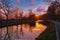 Gold sunset over river with sun rays, tree silhouettes and reflection on water