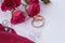 Gold wedding rings on pink fabric with white ribbon and roses