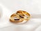 Gold wedding rings rest on a silk-covered table