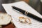 Gold wedding rings on a sheet covered with writing with a black handle and a wrist watch.