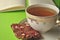 Gold and white porcelain tea cup and saucer with artisan chocolate on bright green background with copy space