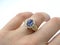 Gold womens ring with diamonds and a blue gem in the form of a flower on a female hand on a white background