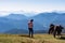 Goldeck - Woman holding baby and playing with herd of wild horses grazing on alpine meadow with scenic view of magical mountain