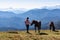 Goldeck - Woman holding baby and playing with herd of wild horses grazing on alpine meadow with scenic view of magical mountain