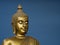 Golden antique buddha statue. The background is light slate gray. The face of the Buddha turned to the right.